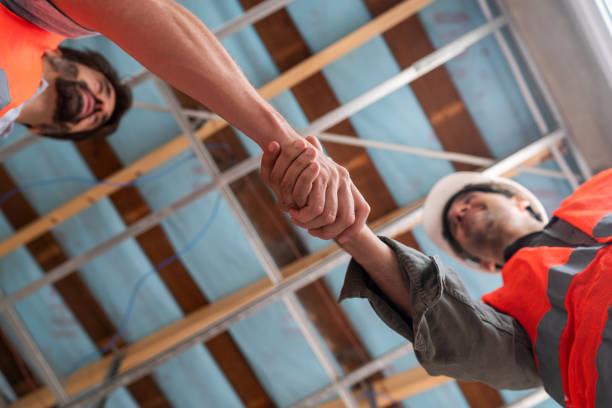 Two construction workers in safety gear engage in a firm handshake, symbolizing teamwork and agreement on a construction site.