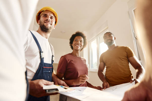 Below view of happy African American couple talking about renovation plans with manual workers at home.