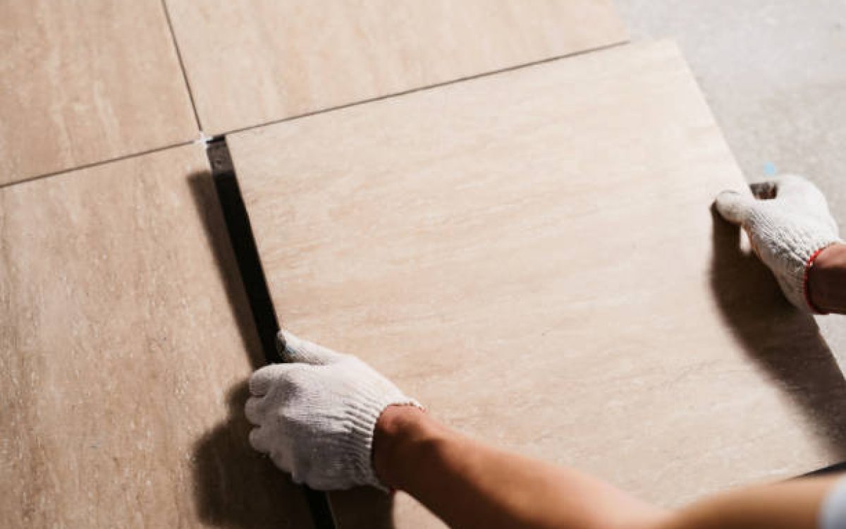 The hands of the tiler are laying the ceramic tile on the floor. Close up macro shot. Home renovation and building new house concept
