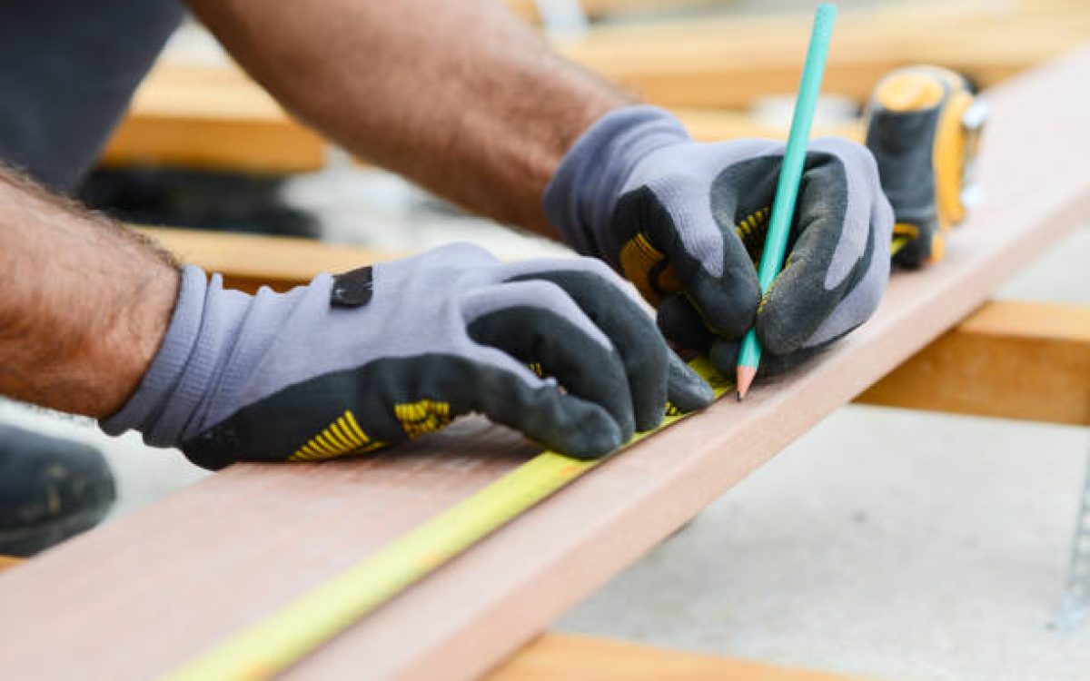 close up detail of manual worker hands working with a measuring tape and pencil in wood plank