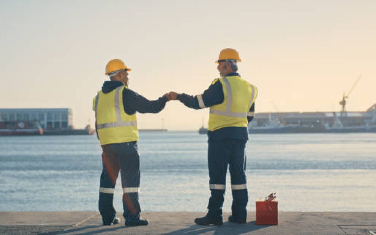 Logistics, delivery and shipping engineers looking motivated and ready with fist bump to build vision for ocean or sea cargo dock. Excited mechanical technicians with? idea for import and export port