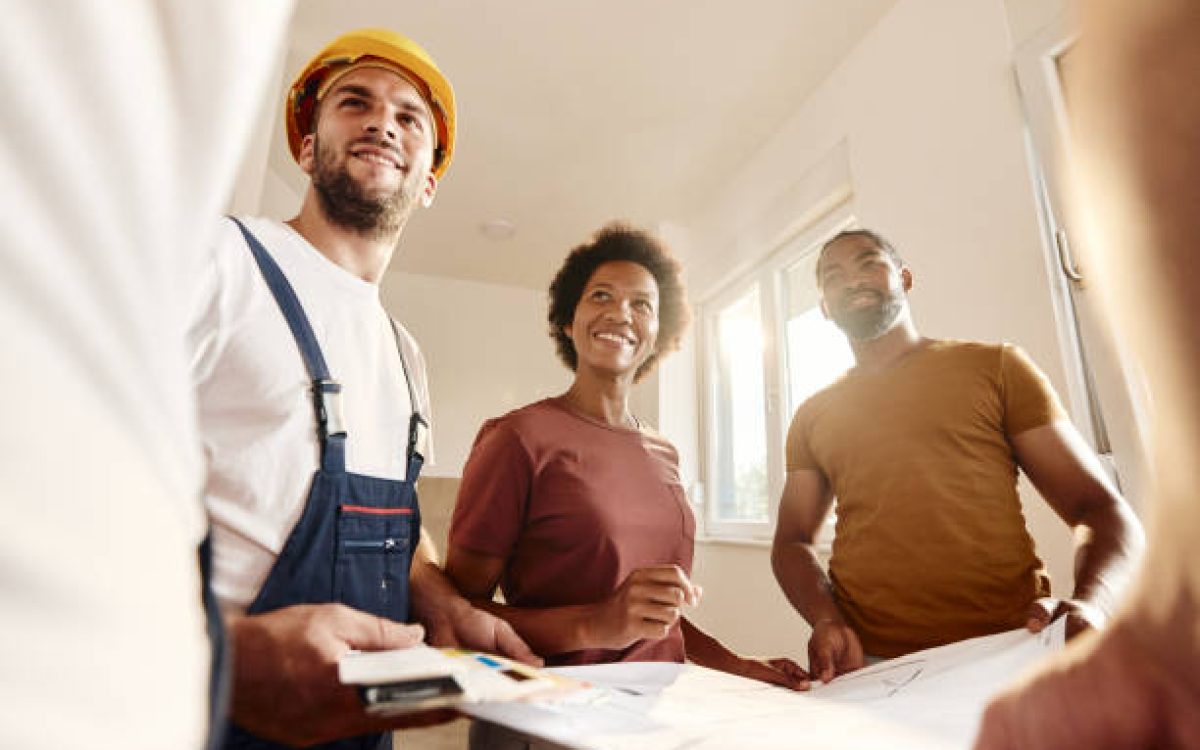 Below view of happy African American couple talking about renovation plans with manual workers at home.
